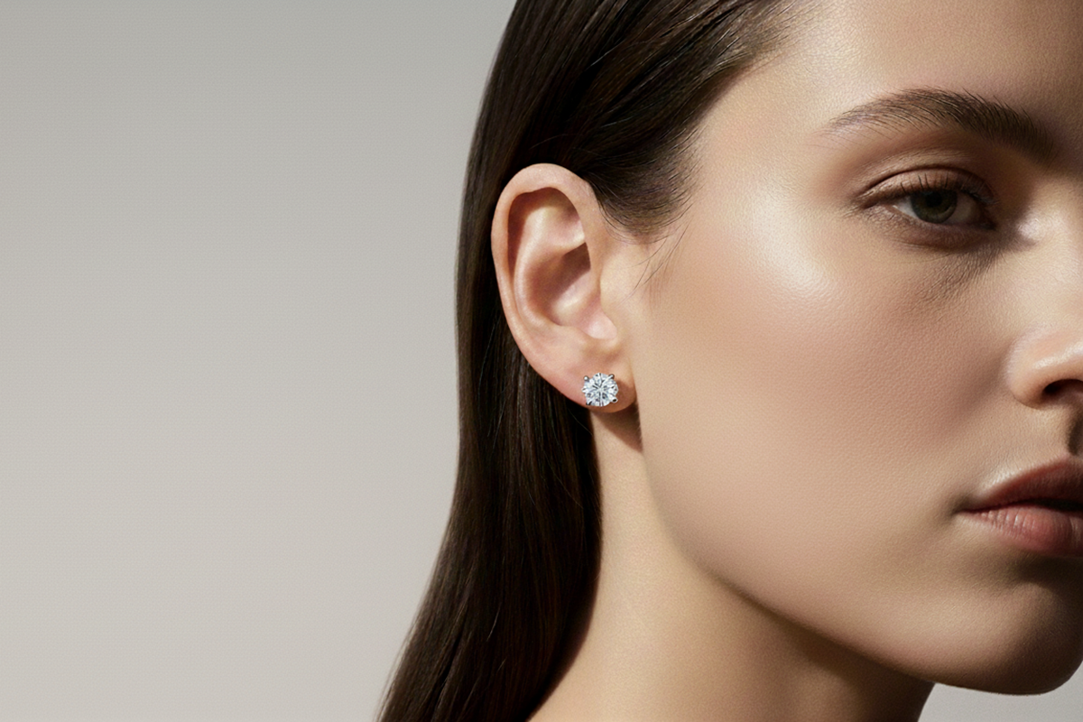 Close-up of a woman wearing round diamond-look stud earrings against a neutral beige background.